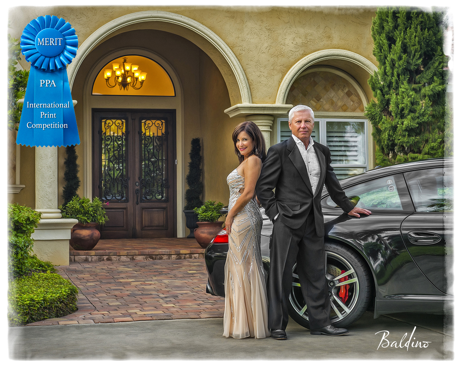 This_is_a_photograph_of_a_man_and_woman_with_their_car. It_is_a_formal_portrait_in_front_of_their_luxurious_home. The_woman_is_wearing_a_gown.